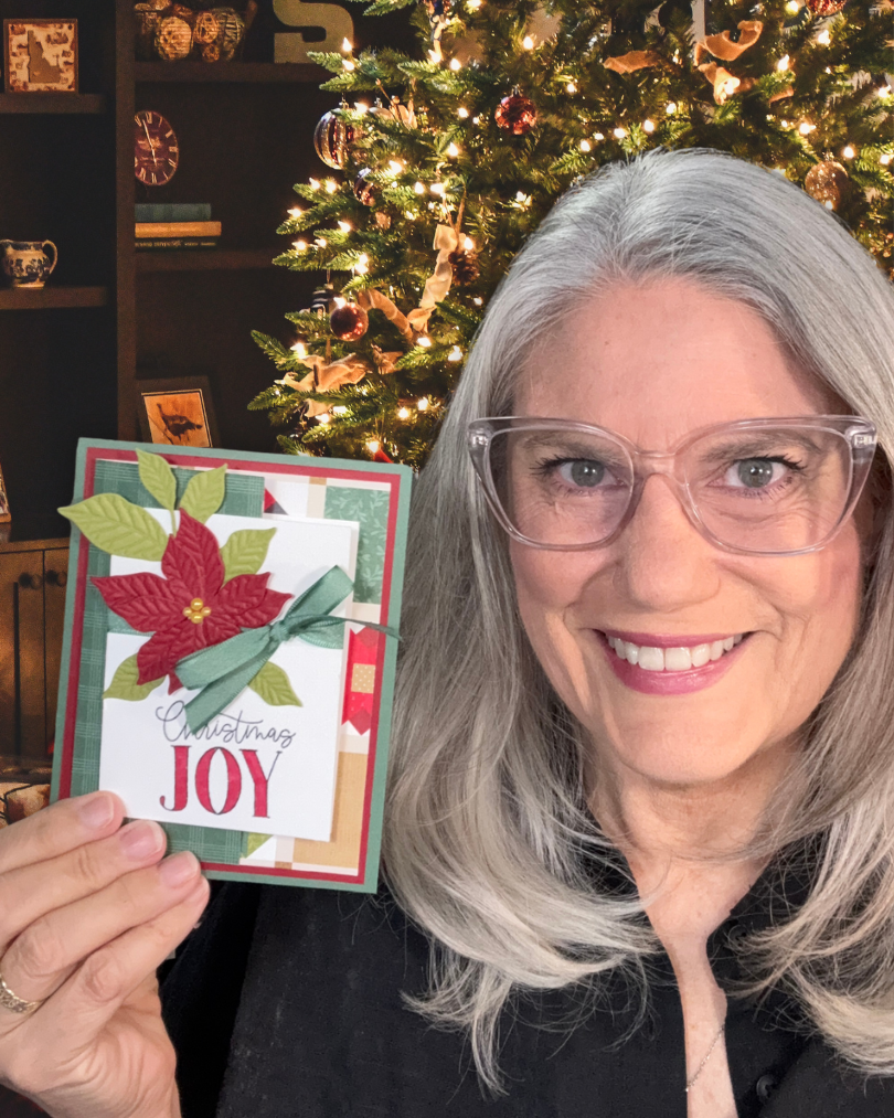 Kristina Rees holding a handmade 6x6 paper Christmas card with a layered poinsettia design.