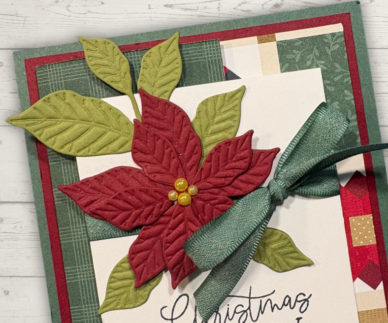 Close-up of the layered poinsettia embellishment with textured petals, pearls, and ribbon on a Christmas card.