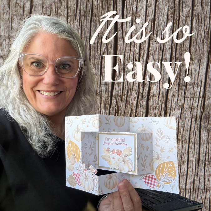 Woman smiling while holding up a finished trifold shutter card decorated with fall leaves and a pumpkin, with the sentiment 'grateful for you this season