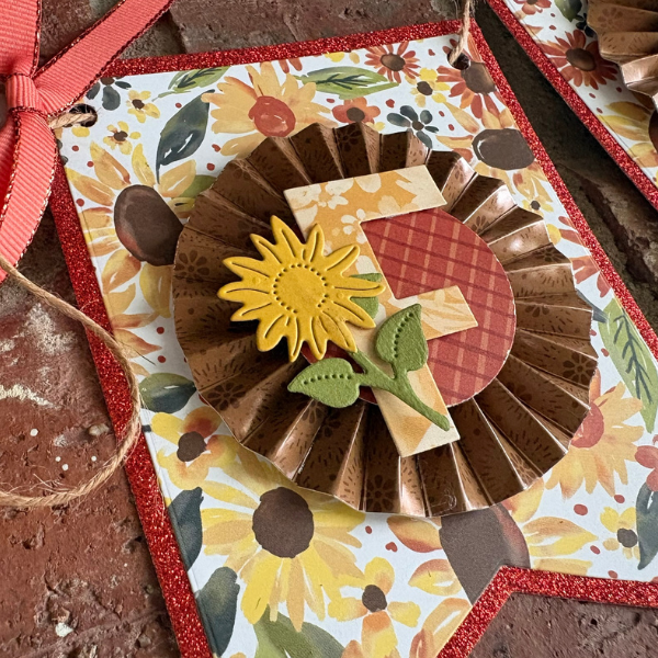 DIY Fall Paper Banner pennant featuring a brown paper rosette, sunflower embellishment, and layered FALL letters.